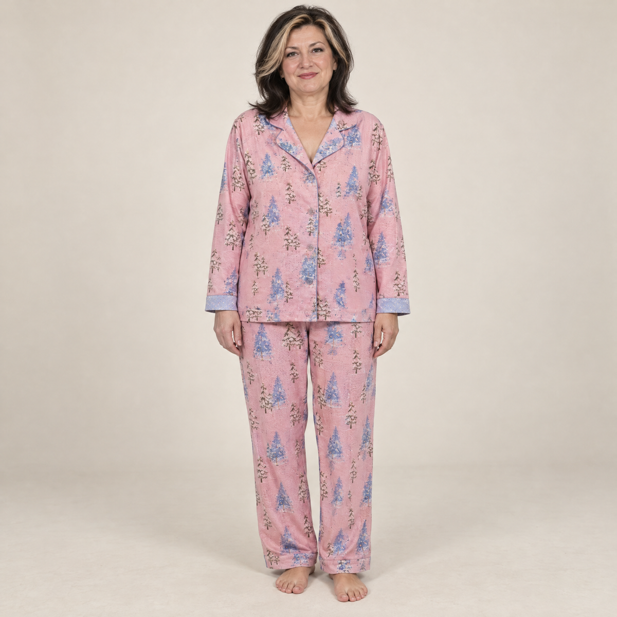 Woman in her 50s wearing pink Christmas tree print cotton flannel pyjamas, full-length front view
