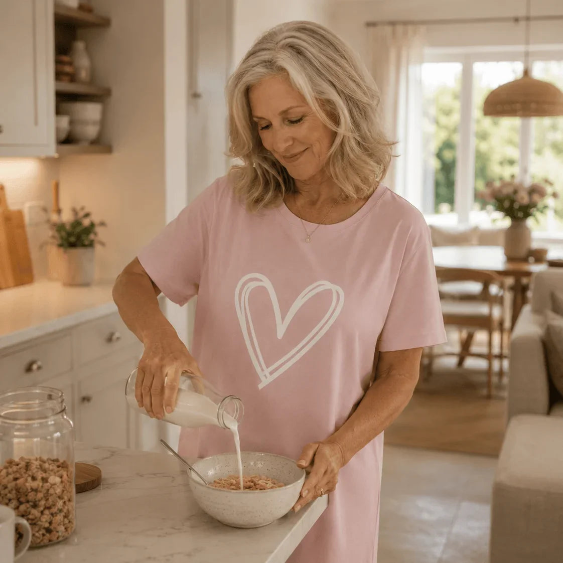 Woman in a pink Night Owl Pyjamas lightweight nightdress with a white heart pouring milk into a bowl.