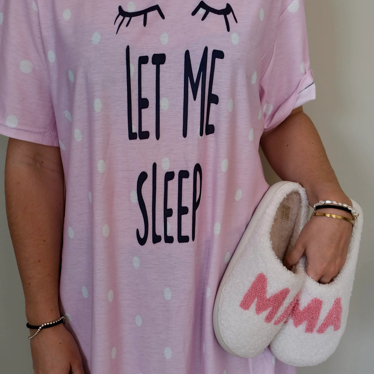 Woman in a pink 'Let Me Sleep' nightdress holding white Night Owl Pyjamas MMA sherpa slippers.